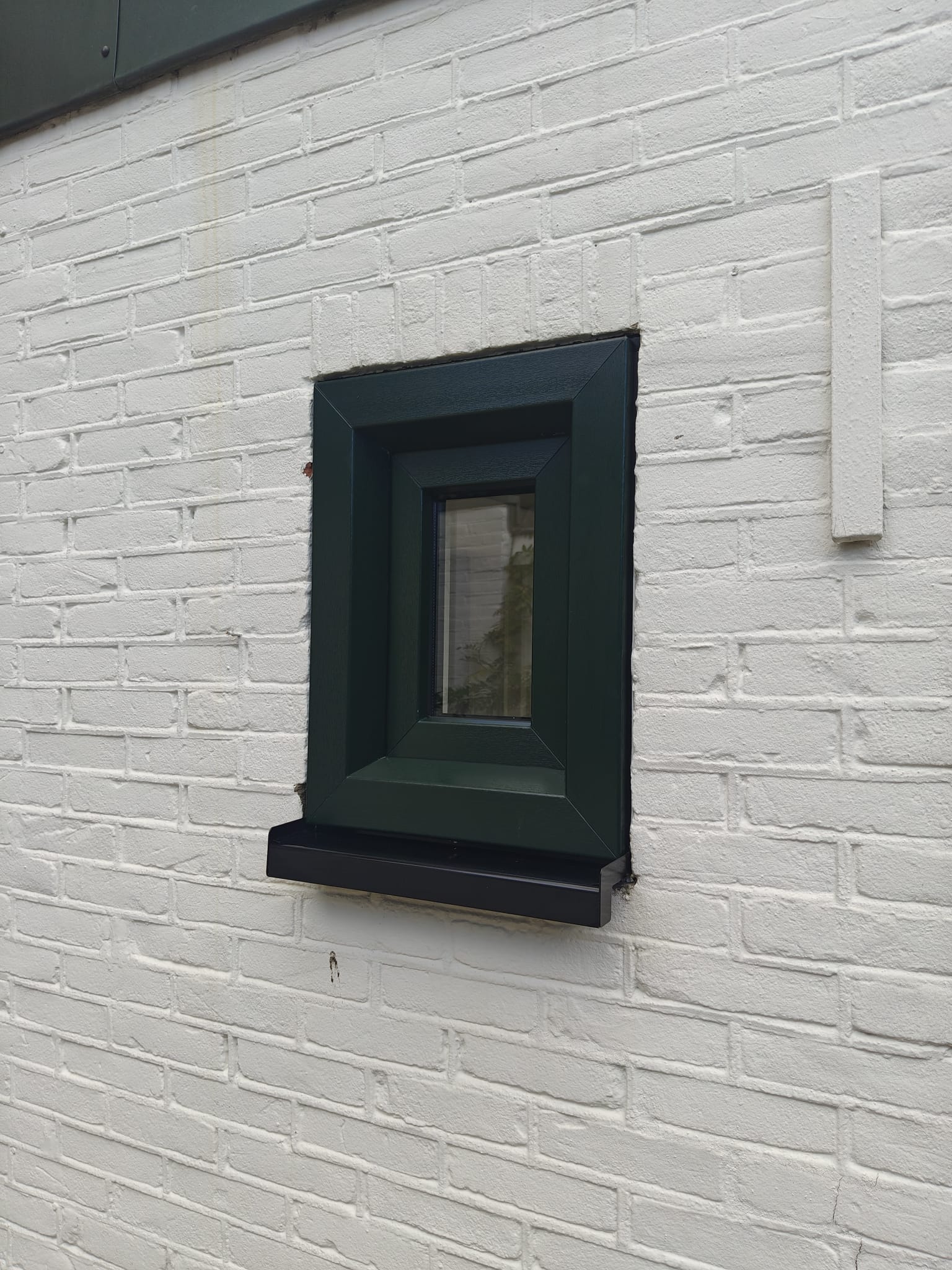 Groen kunststof kiepraam in een witte bakstenen gevel van een jaren-30 woning in Enschede